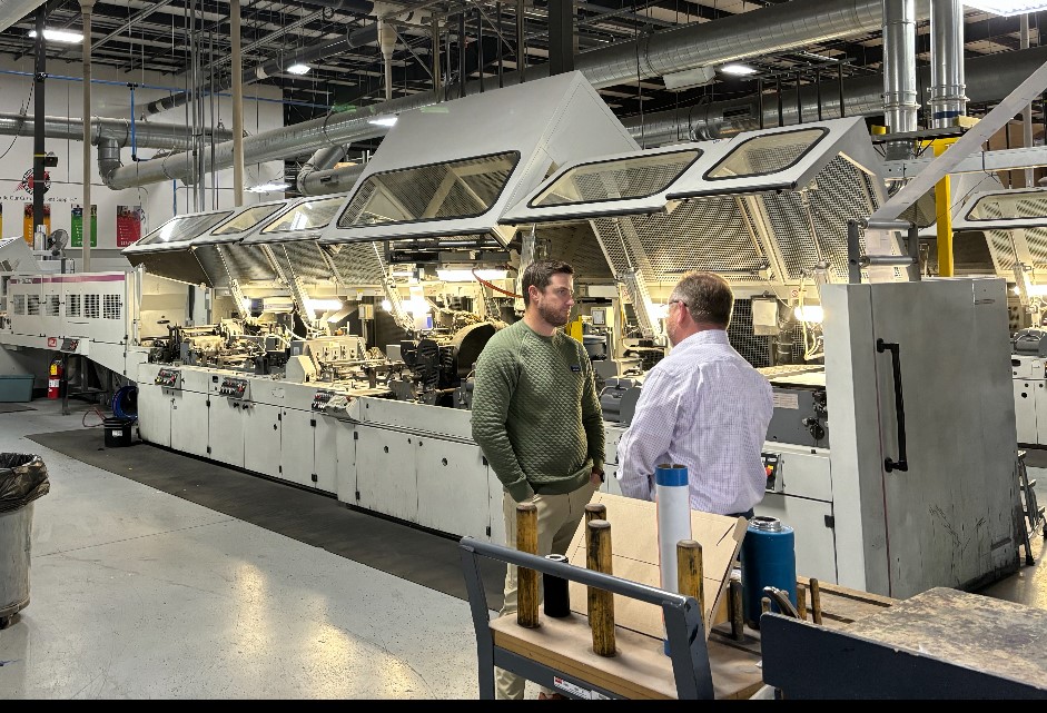 Two men standing next to some equipment in a factory - folding cartons