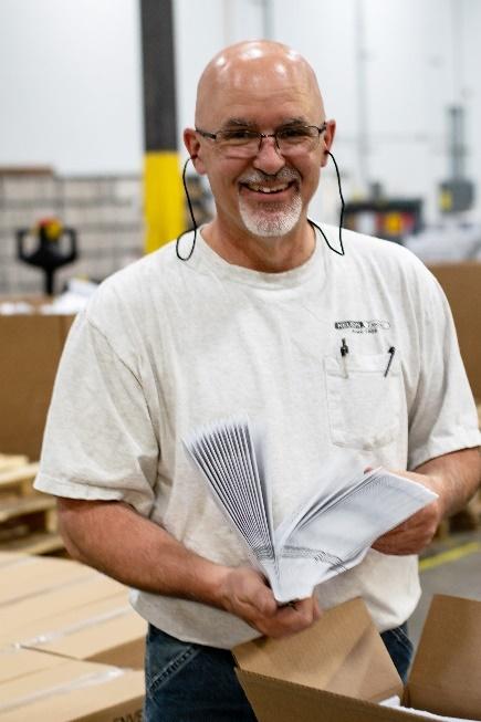 Man smiling holding white envelops in warehouse - sustainable packaging companies